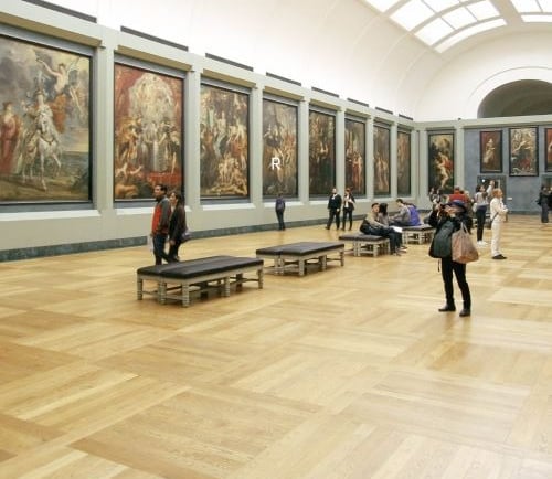 Visitors viewing classic Renaissance paintings in a spacious art museum gallery with hardwood floors.