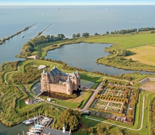 Aerial view of Muiderslot Castle with historic gardens, moat, and boats on the water in Muiden.