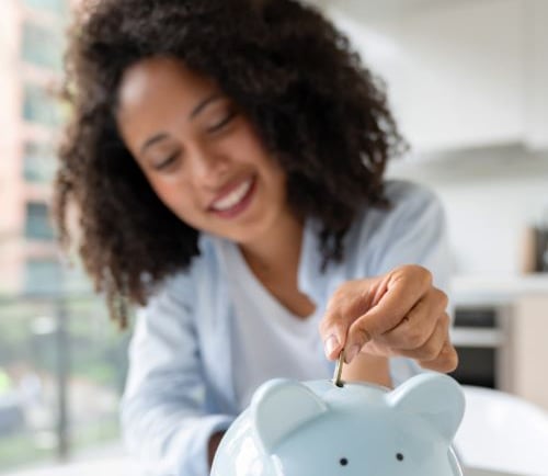 a woman putting coins into a piggy bank
