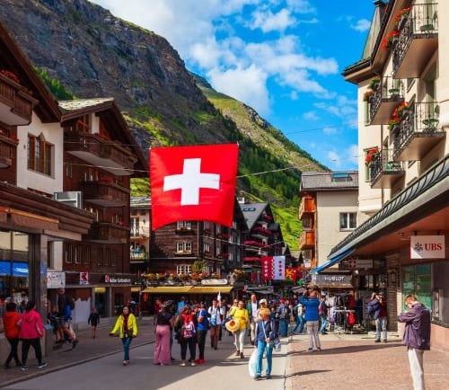 a group of people walking down a street with a swiss flag