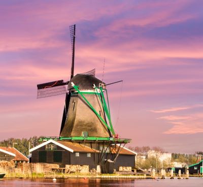Traditional Dutch windmill at Zaanse Schans beside a river under a pink sunset sky.