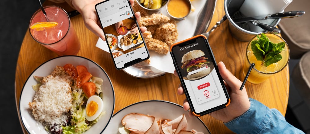 a person holding a cell phone phone in front of a table with food and drinks