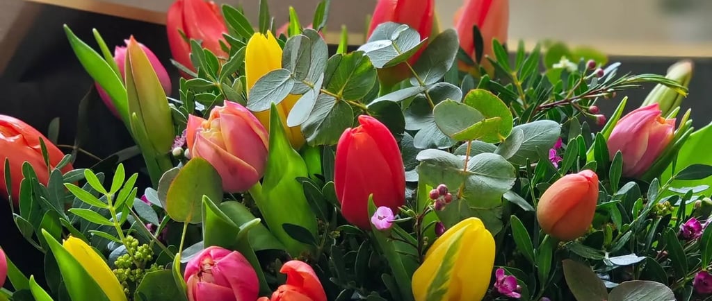 A vibrant bouquet featuring red, yellow, and pink tulips mixed with eucalyptus leaves and small purple flowers