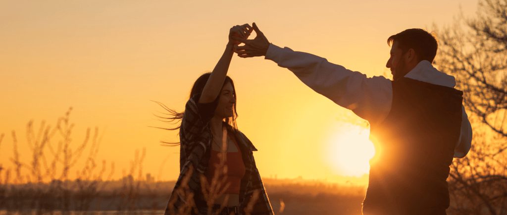 a man and woman dancing at sunset