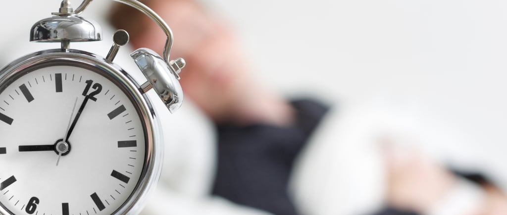 a man laying in bed with a clock on the side of the clock