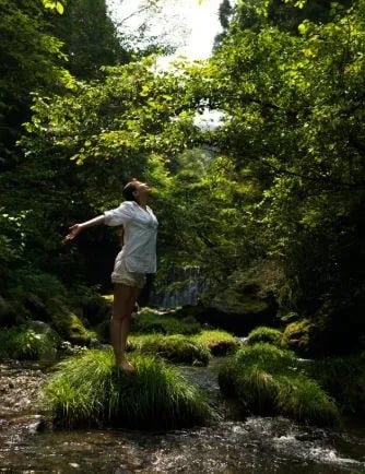 Femme debout en forêt, respirant profondément pour apaiser le stress et se reconnecter à son corps
