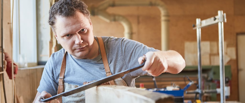 a man in a working on timber with a pair of drawknife