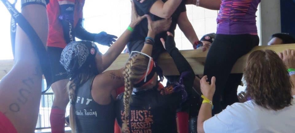 a group of women helping eachother over a wall at an obstacle race