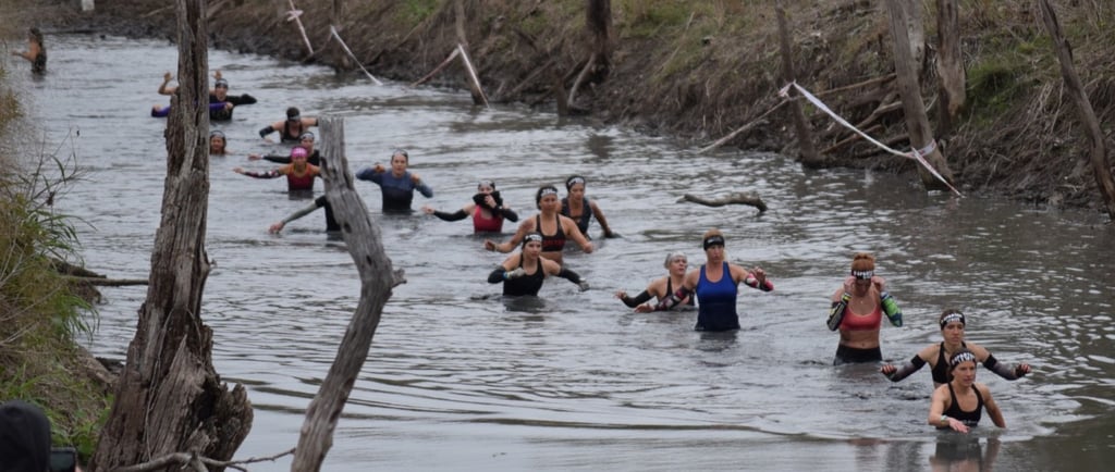 Female elite obstacle racers going through muddy creek obstacle
