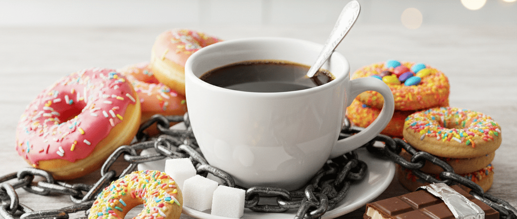 Uma xícara de café com açúcar e doces em cima da mesa, mas cercados por correntes vicio em açúcar