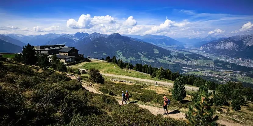 Hikers on a scenic mountain trail overlooking Innsbruck valley and Alps..