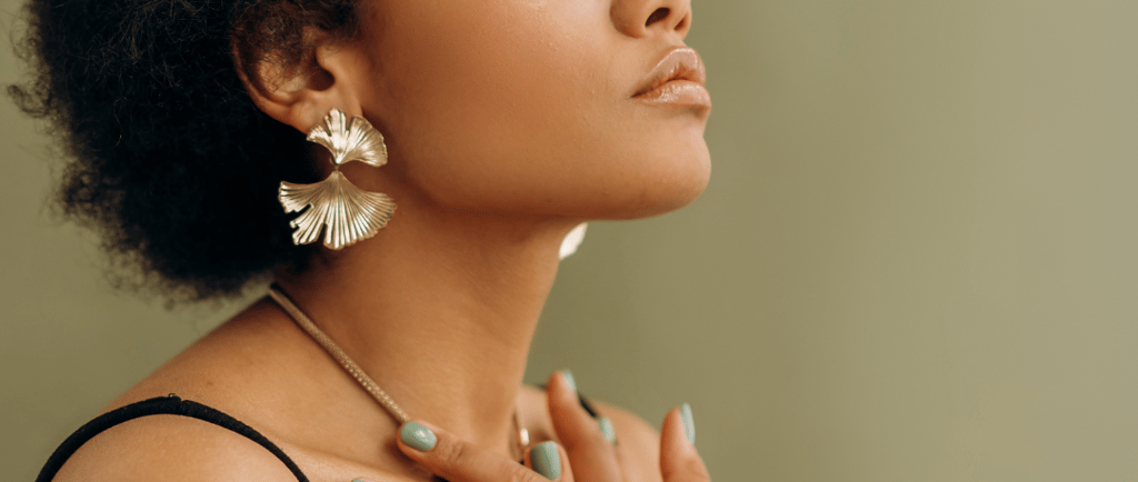 Black woman with afro hair wearing gold statement earrings and a ringset with green manicure.
