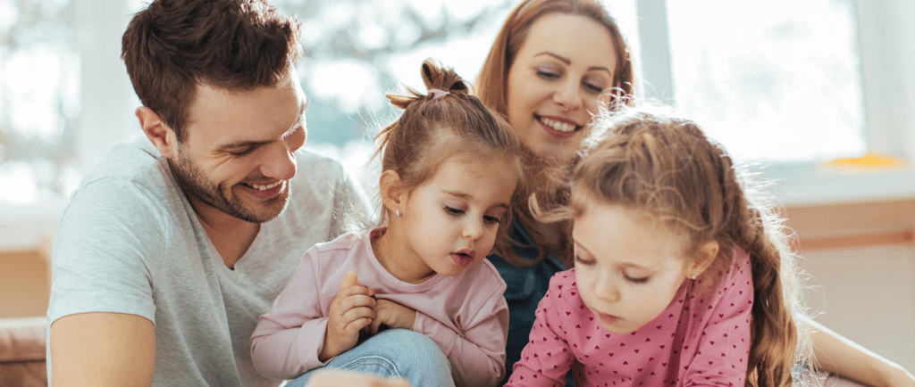 Mother and father reading a book with their two daughters