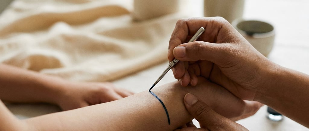 A person applying a blue temporary tattoo or body art ink to a wrist using a fine-tipped metal tool.