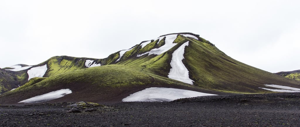 A green mountain with ice falling from the top.