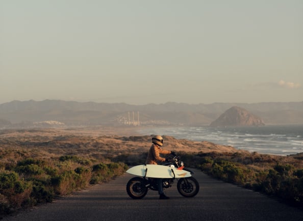 A scenic background with mountains and oceans. A person riding motorbike and scateboard toward it 