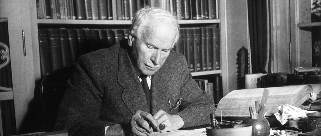 A black and white potrait of Swiss psychatrist Carl Jung sitting in his office writing something.