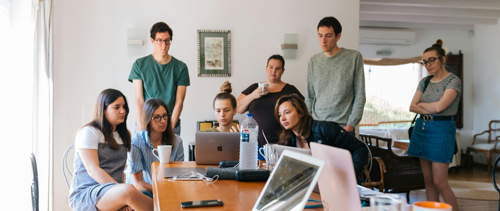 a group of people sitting around a table with laptops