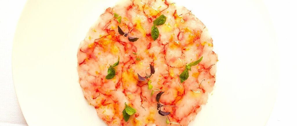 Un plato blanco con un carpaccio de gambas en forma circular