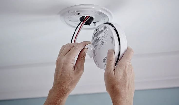a person is holding a white smoke detector in their hands