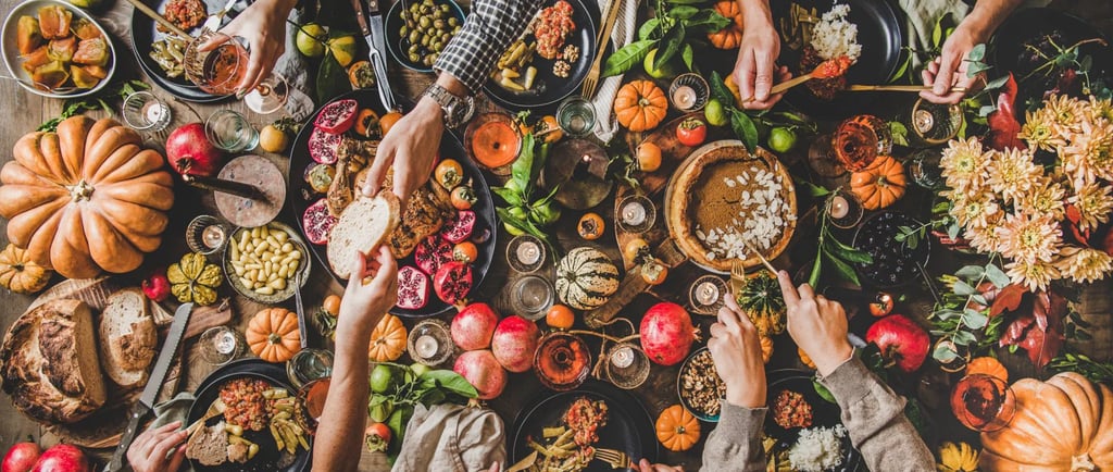 Many hands sharing an abundance of food at the table.
