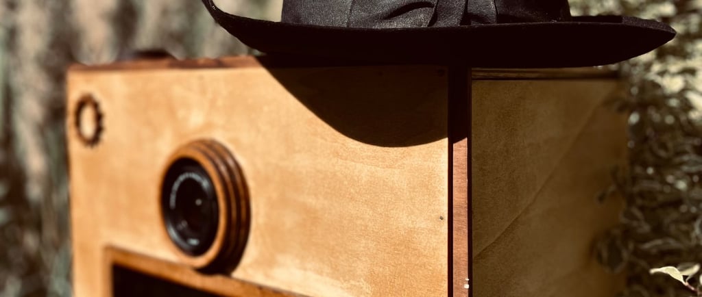 Détail du photobooth en bois vintage avec objectif apparent et chapeau posé, mise en scène poétique