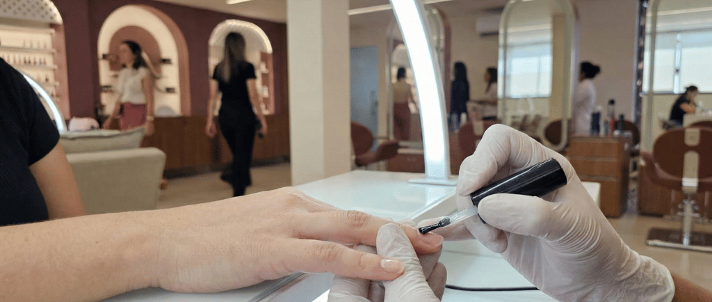 Manicure aplicando gel de blindagem para proteção e fortalecimento das unhas naturais.