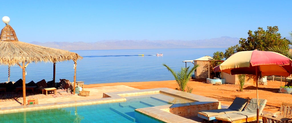 Swimmingpool am Strand mit vorbeifahrendem Boot im Meer