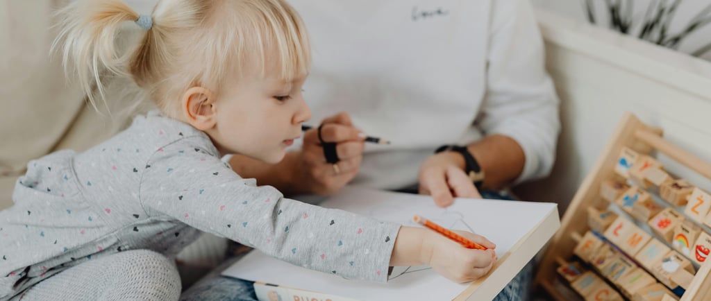 Vaikas su forne matoma mama piešia ant lapo, šalia pastatytos kaladėlės.
