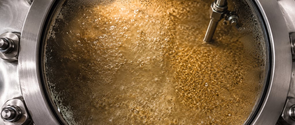 High-solids grain mash fermenting behind a stainless-steel vessel sight glass.