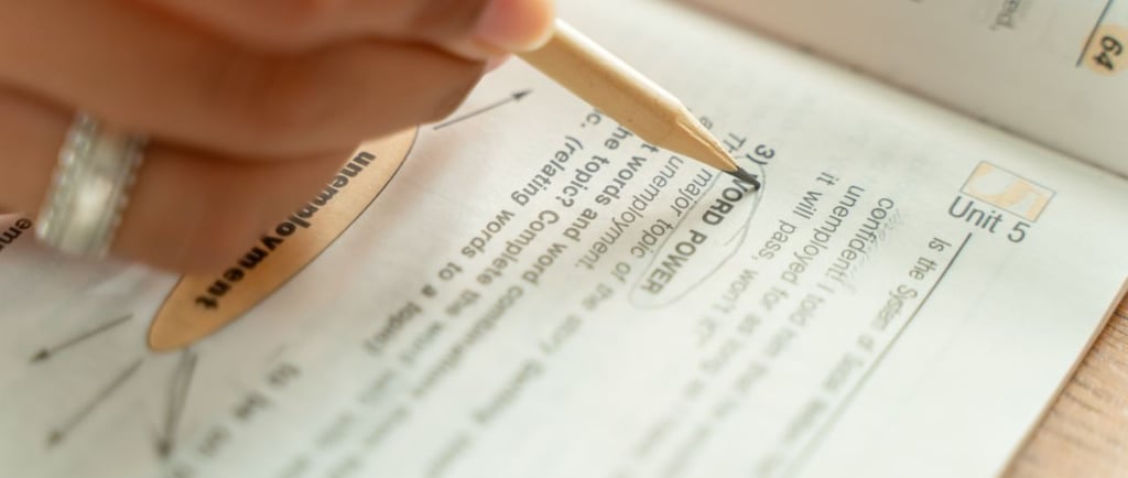 Close-up of a student circling answers in an English language textbook with a pencil while studying.