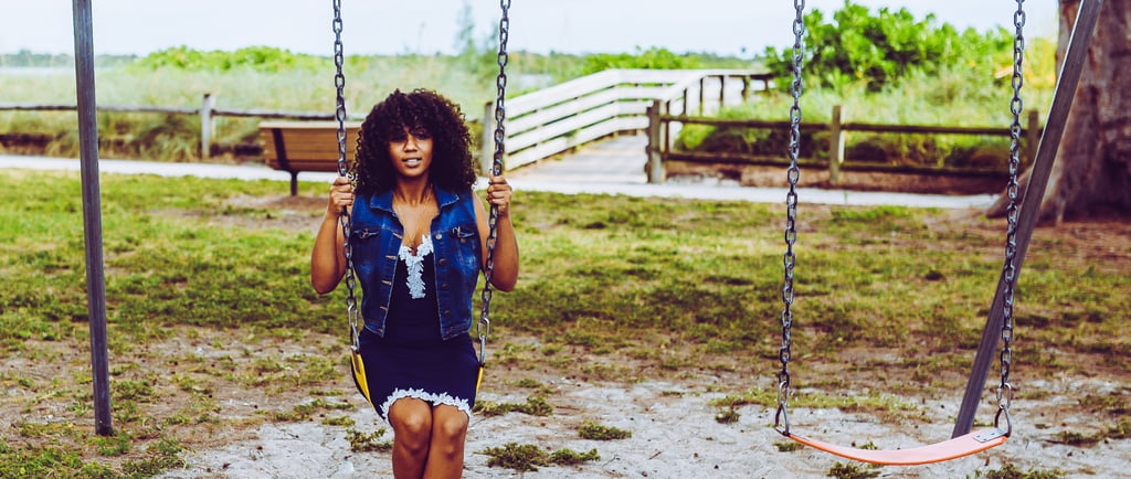 A young woman with curly hair sitting on a playground swing set in an outdoor park.