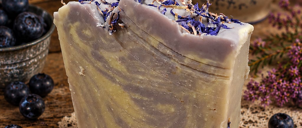 Handmade huckleberry swirl artisan soap bar topped with dried botanicals on a rustic wooden table.