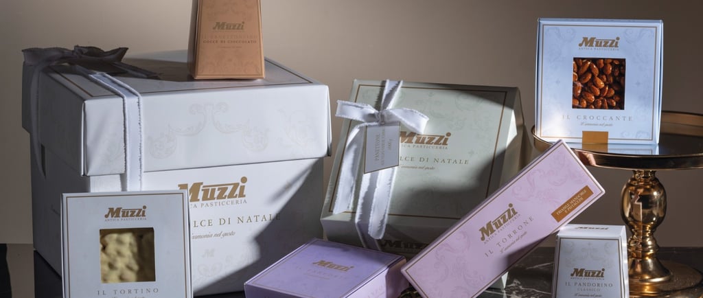 Confezioni e prodotti natalizi del brand Muzzi, parte del Gruppo IDB, rappresentativi della pasticceria italiana di qualità.