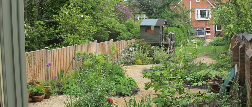 A winding gravel path leads through a lush landscaped backyard garden with flower beds and a wooden playhouse.