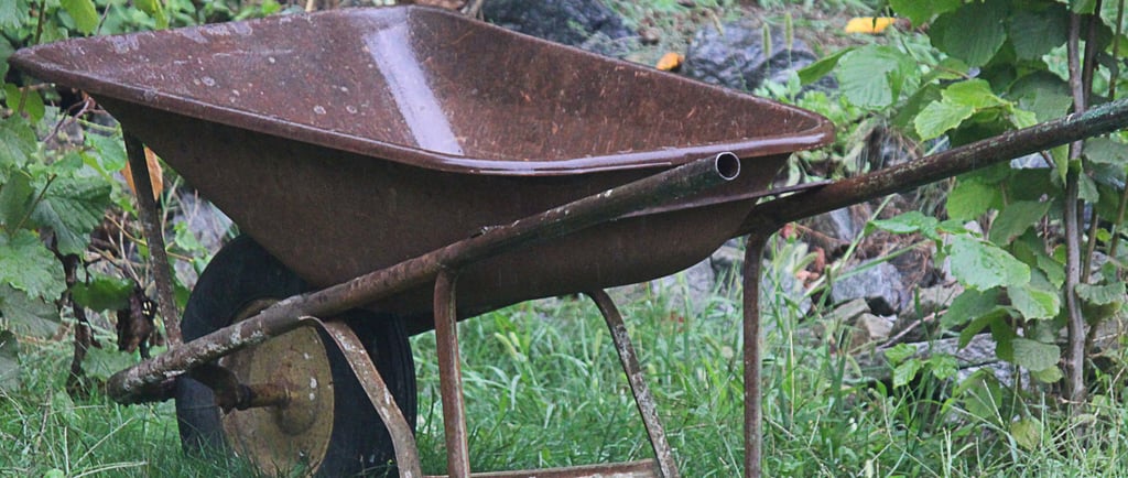 A vintage rusty metal wheelbarrow sitting on a green grassy lawn in a garden setting.