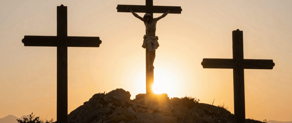 A group of people are gathered around a baptismal font inside a church. They appear to be celebrating an event, possibly a baptism. The setting includes colorful stained glass windows, one depicting a religious figure, and a lit candle on the wall.