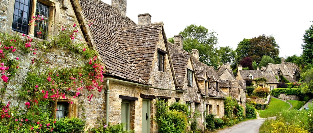 Historic stone weaver cottages with gabled roofs and flowers at Arlington Row in Bibury, Cotswolds.