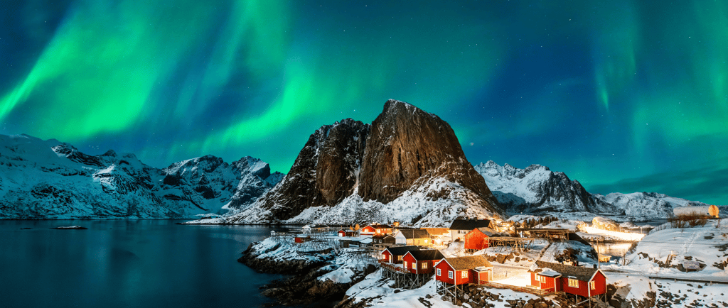Green Northern Lights aurora borealis over a snowy fishing village in Lofoten Islands, Norway.