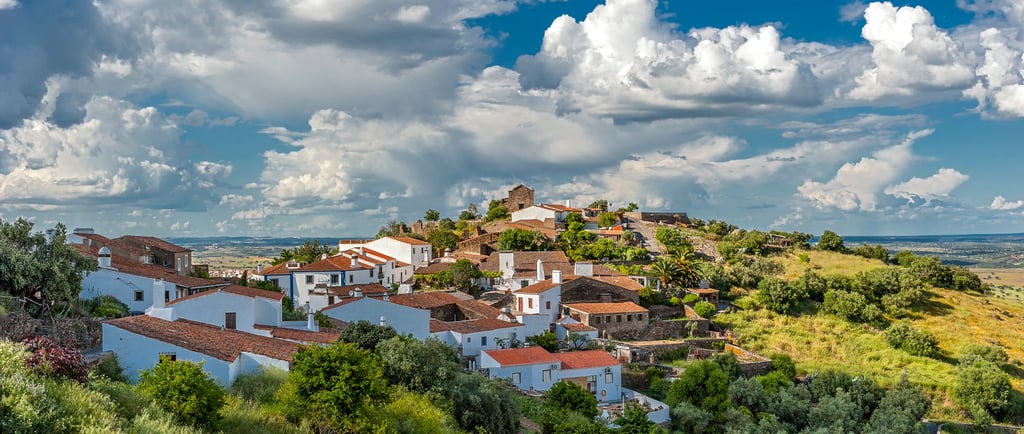 Panoramic view of white houses in a traditional Portuguese village under a cloudy blue sky.