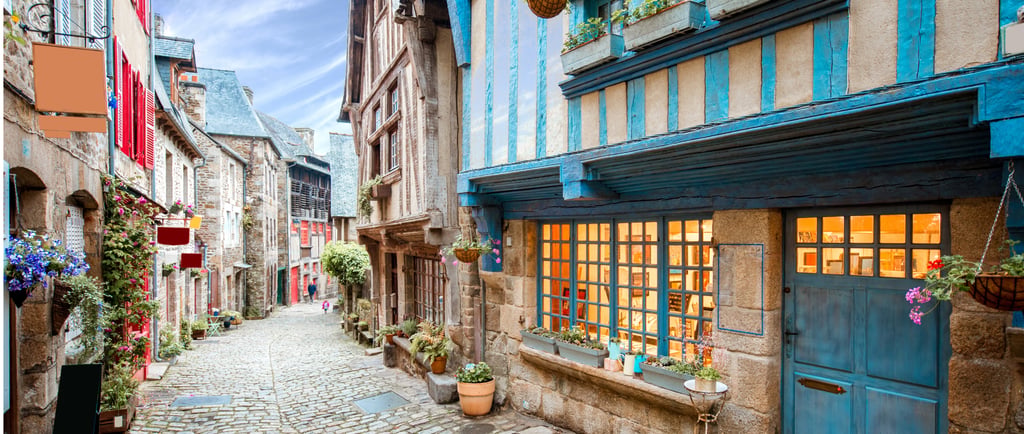 Charming cobblestone street in Dinan, France with blue half-timbered houses and flower boxes.