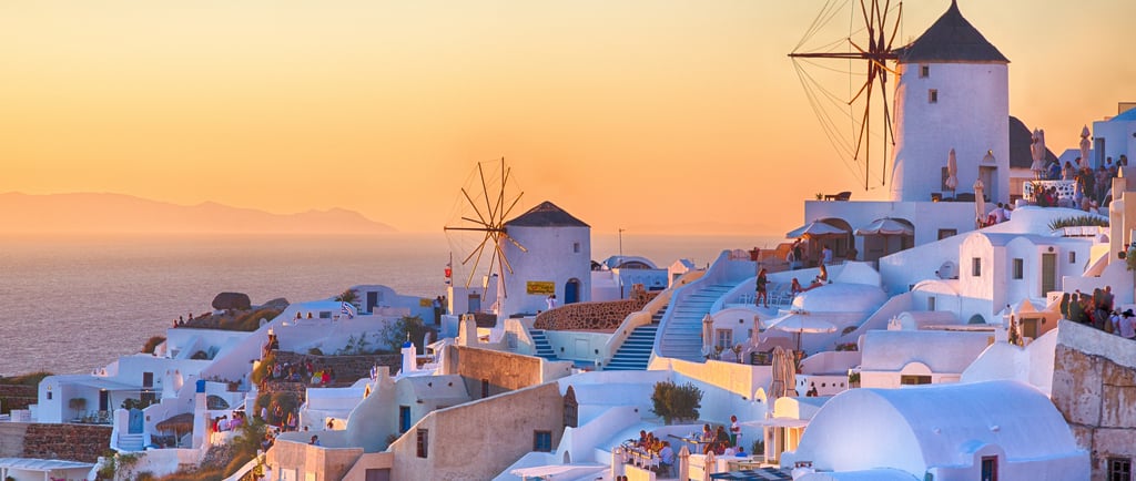Traditional white windmills and houses in Oia, Santorini overlooking the Aegean Sea at sunset.
