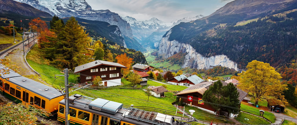 Yellow Swiss train traveling through Wengen village overlooking the Lauterbrunnen valley and Alps.