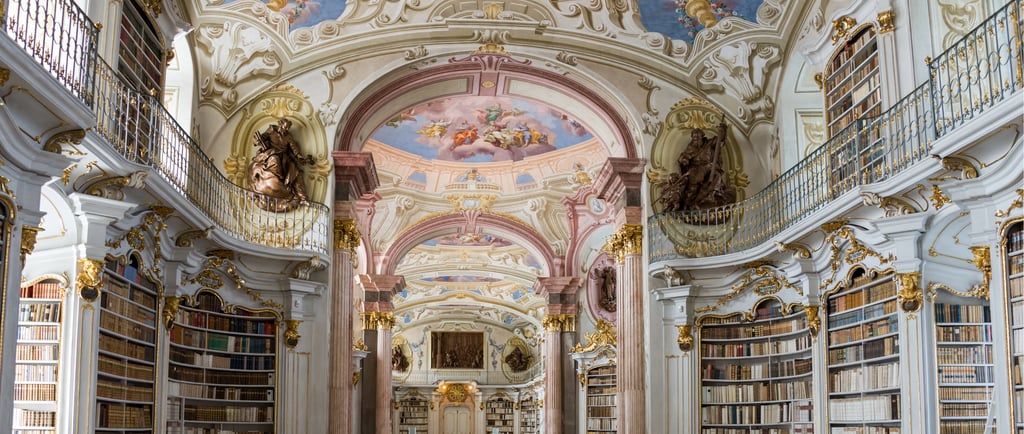 Ornate Baroque architecture of the Admont Abbey Library featuring ceiling frescoes and gold accents.