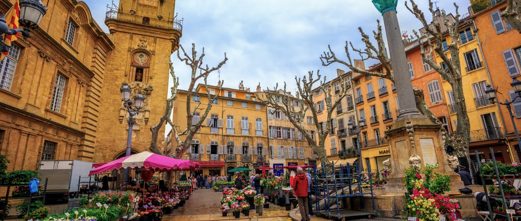 Outdoor flower market in Aix-en-Provence square with historic clock tower and colorful French buildings.