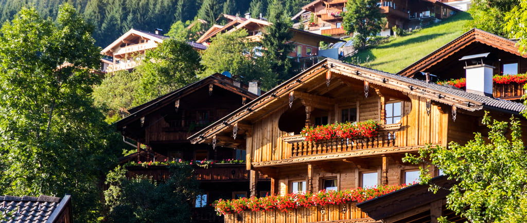 Traditional wooden Swiss chalets with red flower boxes nestled on a lush green mountain slope.