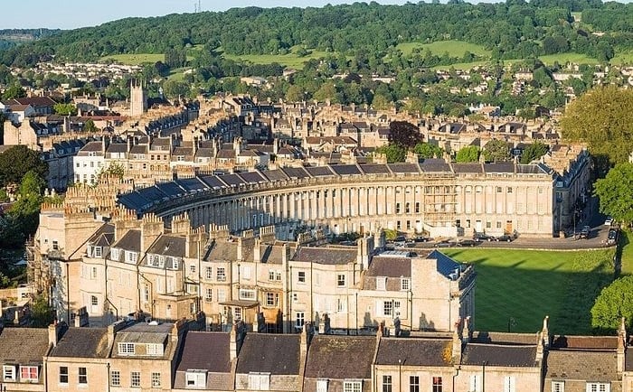 Aerial view of the historic Royal Crescent in Bath, England, featuring Georgian architecture and lush green hills.