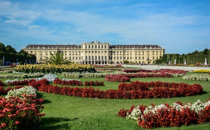 Schonbrunn Palace in Vienna with vibrant flower gardens under a clear blue sky.