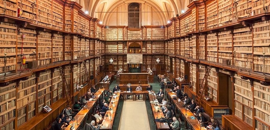 People studying at long tables inside the historic Casanatense Library with massive wooden bookshelves.
