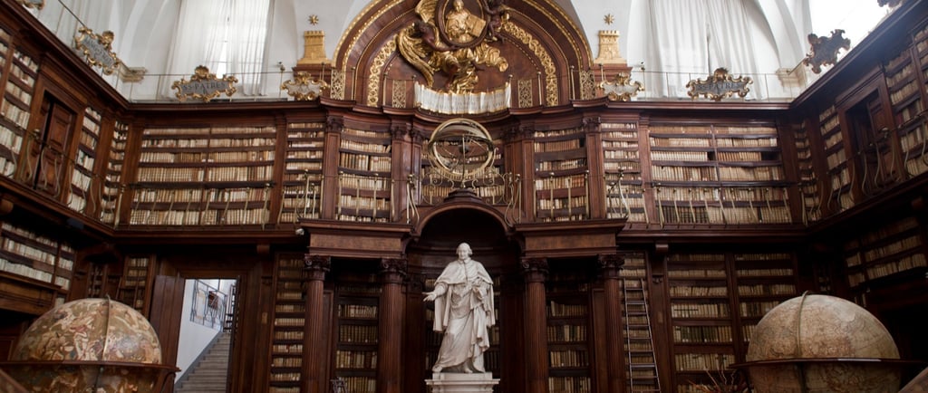 Ancient ornate library with floor-to-ceiling wooden bookshelves, marble statues, and antique globes.